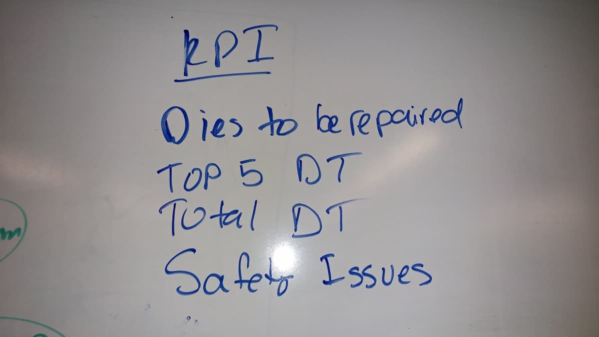 Four KPIs written on a whiteboard in blue marker: dies to be repaired, top five downtime, total downtime, safety issues.